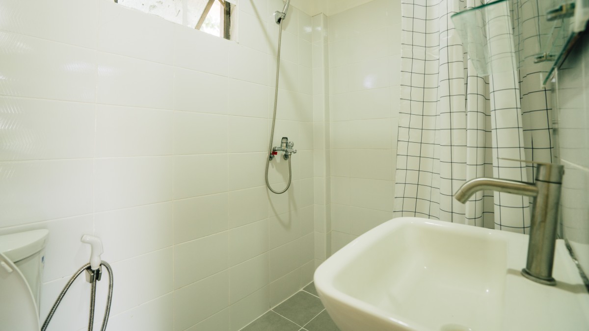 白のタイルで統一され、チェック柄のシャワーカーテンや最新の洗面台・トイレが機能的に配置されたEnglish Fella 2の清潔なドミトリー（寮内）バスルーム空間
