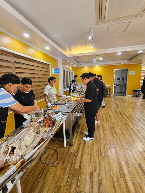 多国籍な留学生がビュッフェ形式で食事を楽しむCIP English Academyの清潔な食堂風景とフィリピン伝統料理レチョン