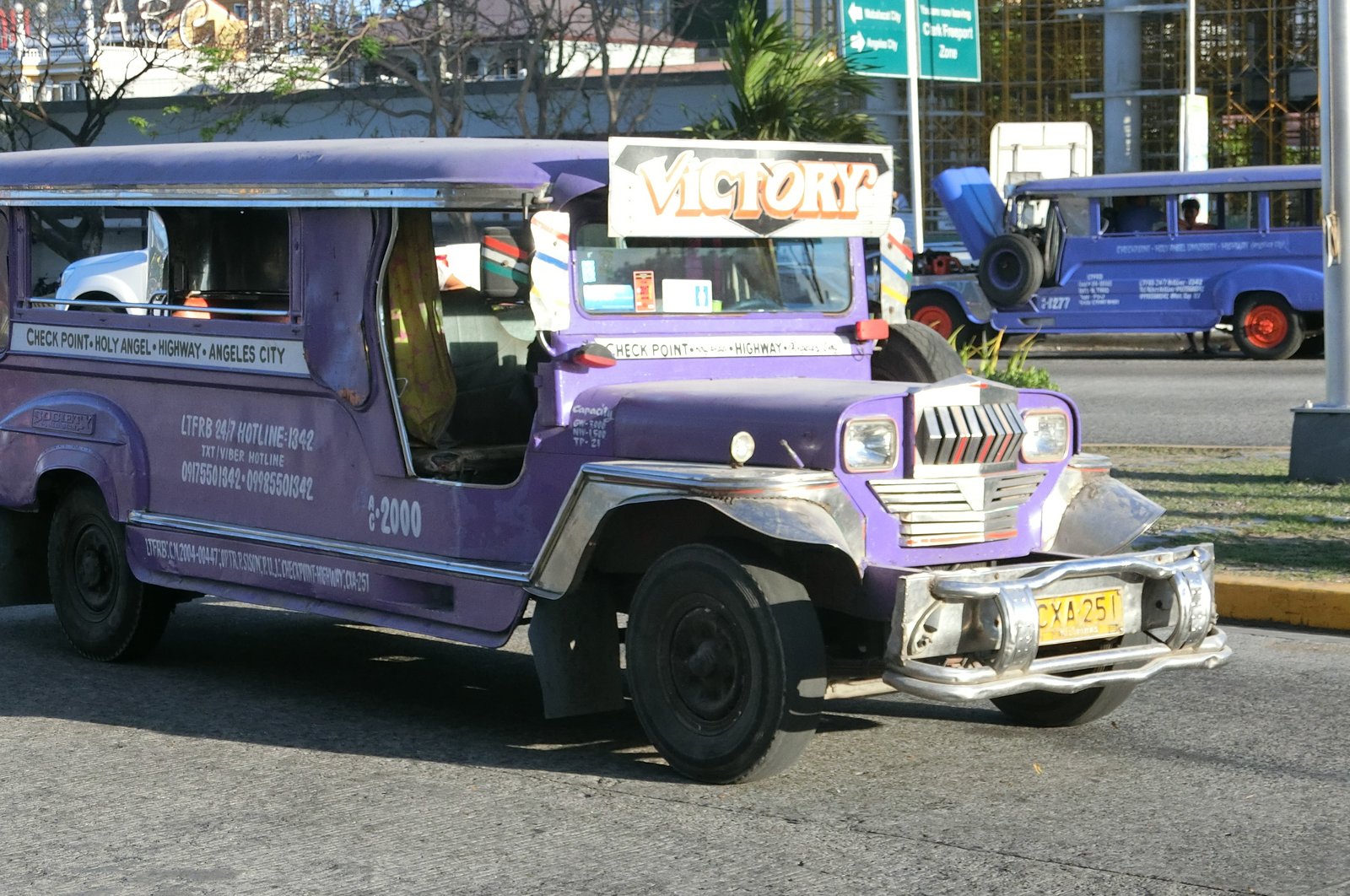 クラークの街を走る紫色のジプニー。車体に行き先が書かれ、奥にクラーク経済特区を示す道路標識が見える