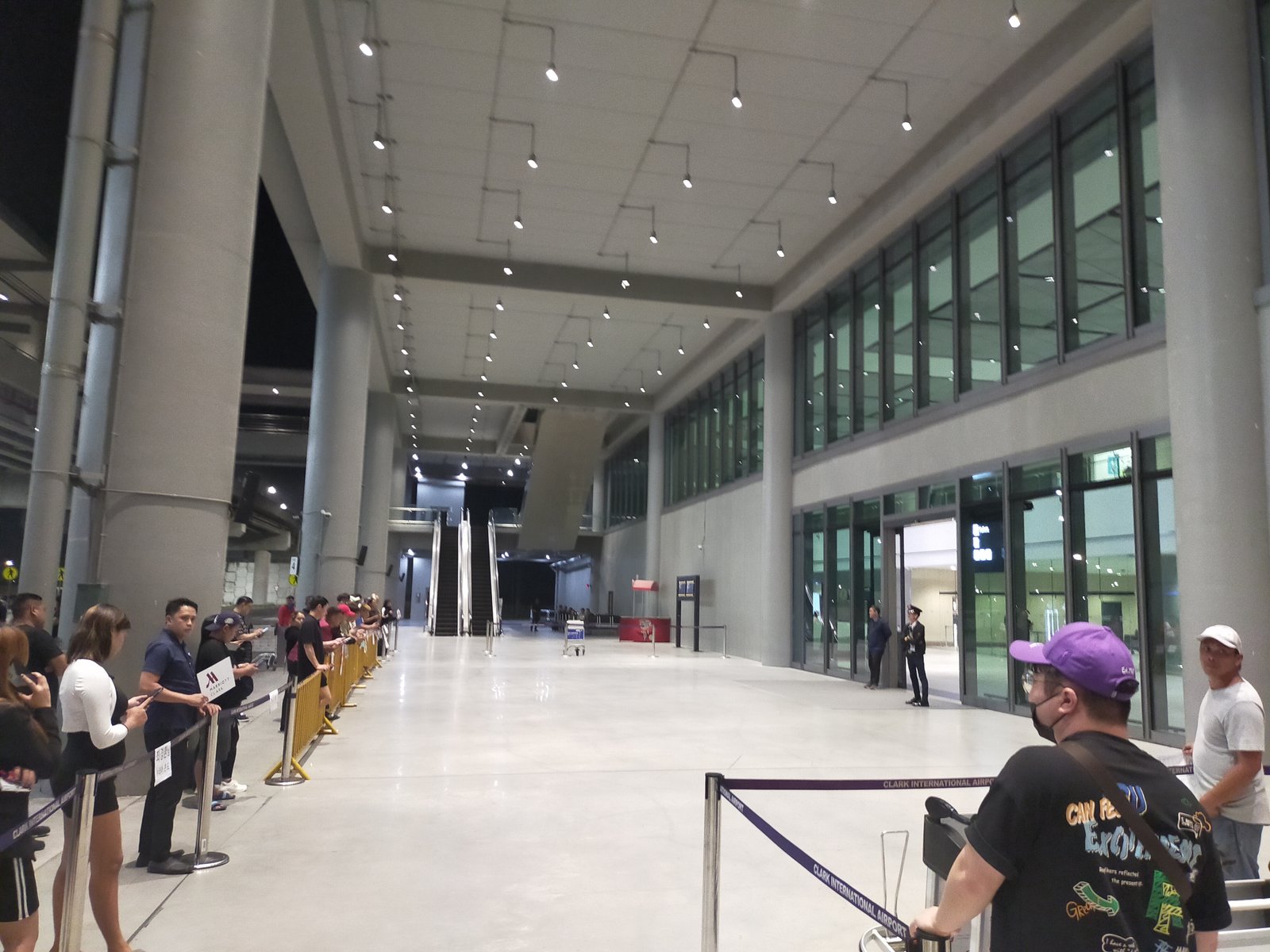 クラーク国際空港の到着口。出迎えの人がロープの外側に並び、正面にエスカレーターが見える